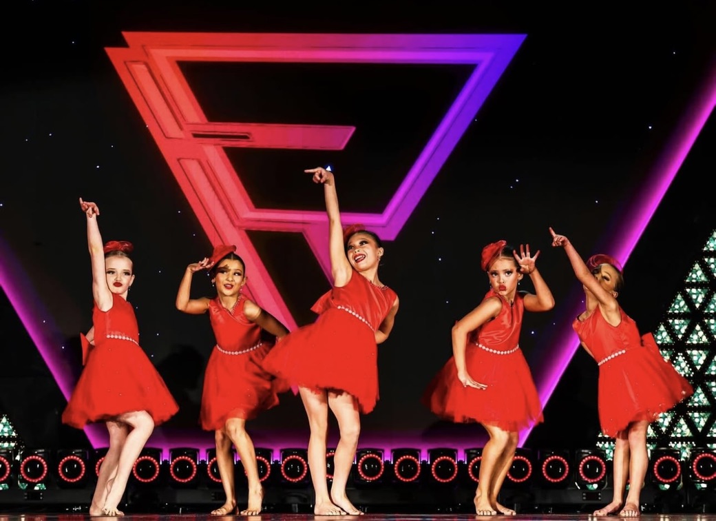 Five dancers in red costumes performing together on stage