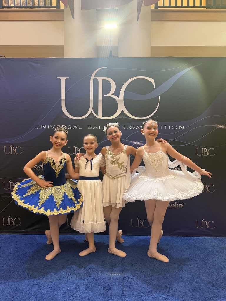 Four young dancers in ballet costumes standing together in front of a Universal Ballet Competition backdrop