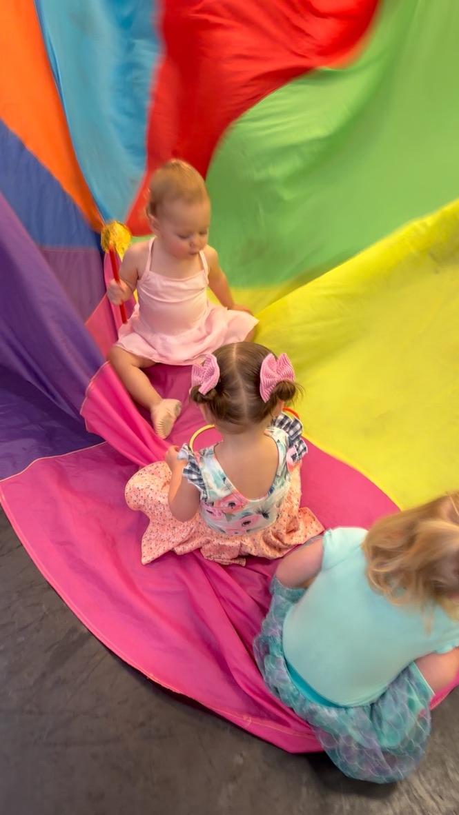Three young dancers sitting together on a colorful parachute during class