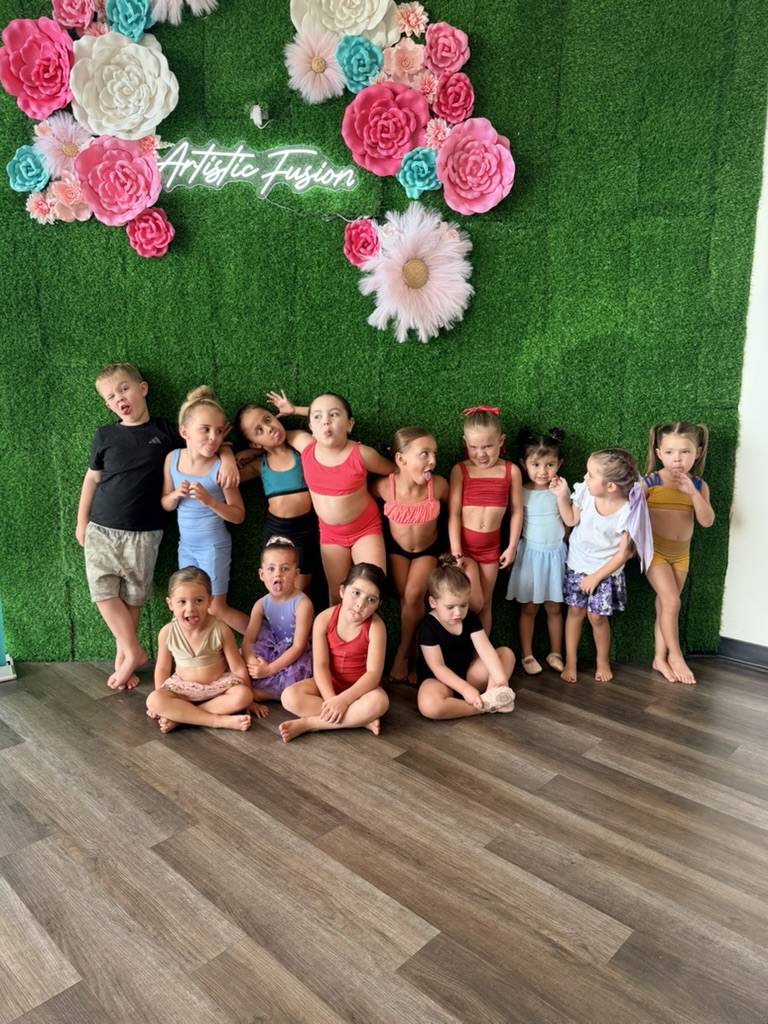 A group of young dancers posing together in front of the Artistic Fusion flower wall
